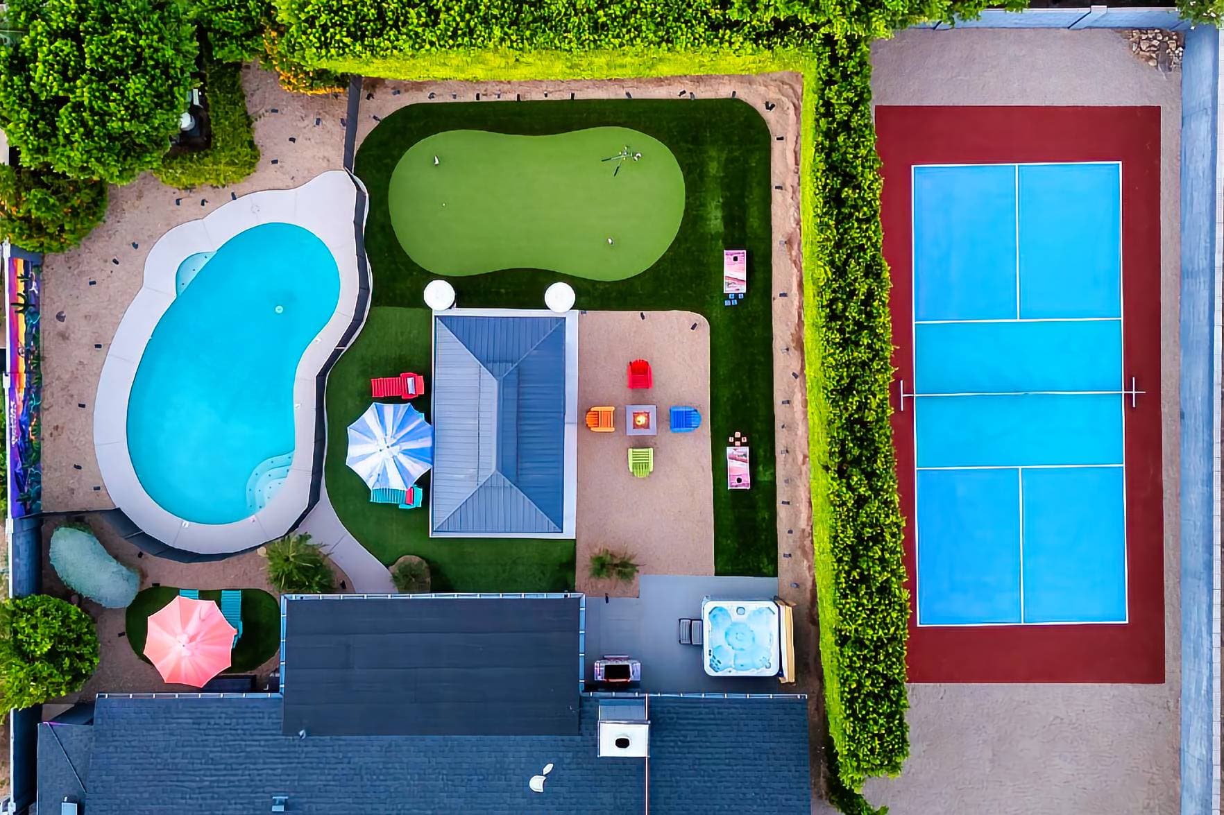 Aerial view of the backyard oasis featuring a heated pool with safety gate, 6 poolside lounge chairs, pickleball court, hot tub, fire pit, gazebo,  3-hole putting green, custom mural, grill, cornhole, ping pong, patio heaters & 50 LED solar lights.